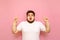 Portrait of shocked overweight man on pink background, looks into camera with surprised face and shows hands up on copy space.