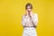 Portrait of shocked or scared young woman with fair hair in casual beige blouse, isolated on yellow background