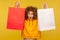 Portrait of shocked shopper, amazed curly-haired girl in hoodie raising shopping bags with blank area