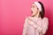 Portrait of shocked woman. Astonished girl stands isolated on pink studio background. Female wears rose clothes looks aside,