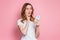 Portrait of a shocked young girl looking at phone and reads a messages or news  over pink background. Surprised woman in a