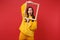 Portrait of shocked young woman in yellow fur sweater keeping mouth wide open, hold picture frame isolated on red