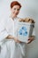 Portrait of a short-haired woman holding a small recycle bin stuffed with paper