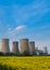 Portrait shot of cooling towers of a coal fuelled power station in the foreground is a bright yellow field of blooming