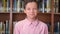 Portrait shot of the cute schoolboy standing near the bookshelf in the library