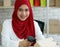 Portrait shot of cute smiling young teenage Muslim woman wearing red hijab sitting on a chair and scanning boxes with barcode