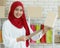 Portrait shot of cute smiling young teenage Muslim woman wearing red hijab standing while holding postage boxes and order
