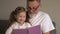 Portrait shot of the grandfather in glasses and cute teen granddaughter reading a book together while sitting on the