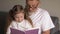Portrait shot of the grandfather in glasses and cute teen granddaughter reading a book together while sitting on the