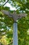 A portrait shot of an old, bird shaped, outdoor, cement lighting post, with a wide wing span, located in a Thai public park.