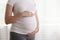 Portrait shot of young beautiful woman on third trimester of pregnancy. Close up of pregnant female with arms on her round belly.