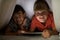 Portrait of siblings under bed sheet using digital tablet on bed