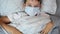 A portrait of a sick caucasian boy lying in bed in medical protective mask getting out from under the covers, blanket, illness and