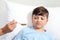 Portrait of sick child lying in ben in hospital room and nurse giving him medicine with spoon