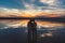 Portrait, silhouette of happy couple watching the colourful bright sunset standing in large lake and kissing, reflection in the wa