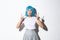 Portrait of silly and cute asian girl in blue wig, squinting and making funny faces, showing peace gestures, standing