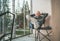 Portrait of a sincerely smiling Middle-aged man dressed open cardigan, jeans, and warm socks sitting in chair on forest house