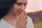 Portrait of a single woman praying and looking down at sunset. Hands folded in prayer concept for faith