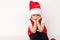 Portrait of sitting resentful little child in red Santa Claus hat isolated on white background. Beautiful five-year European boy.
