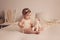 Portrait of a six-month girl sitting on a bed with a toy