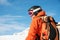 Portrait of a skier in an orange overall with a backpack on his back in a helmet stands against the background of a
