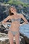 Portrait of skinny young woman in bikini on rocky seashore