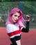 Portrait slim sensual girl cheerleader with pink hair and blue eyes in sportswear posing outdoors near fence at stadium