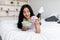 Portrait of slim young Indian lady eating cereal with milk while lying on bed at home, full length
