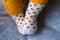 A portrait of small cute baby feet wearing white socks with orange hearts on them. They are resting on a grey pillow and the