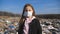 Portrait of small female child in medical protective mask looks into camera against the background of dirty garbage dump