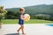 Portrait of small toddler girl with ball walking outdoors in backyard garden.