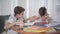 Portrait of smart Caucasian boy doing homework as his brother sleeping on the table. Boy waking up his sibling and