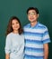 Portrait of a smiley happy loving Asian couple dressed casually standing relaxedly, smiling to a camera for studio shot over green