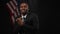 Portrait of smiling African American male politician greeting public in camera flashes with USA flag at black background