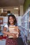 Portrait of smiling african american schoolgirl carrying stack of books in school library