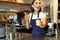 Portrait of smiling asian girl barista, giving out order in cafe, inviting guest to pick up takeaway order near counter