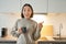 Portrait of smiling asian girl standing in kitchen, drinking coffee from cup and pointing at banner, showing letting