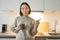 Portrait of smiling asian girl standing in kitchen, drinking coffee from cup and pointing at banner, showing letting