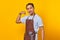 Portrait of smiling Asian young man wearing apron Showing arm muscles while smiling proudly on yellow background