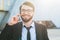 Portrait of smiling bearded businessman in suit using smartphone on office build and sunlight background.