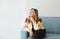 Portrait of smiling beautiful middle-aged woman with blonde hair sitting on sofa at home, holding chin on hand