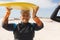 Portrait of smiling biracial retired senior woman carrying surfboard on head at sunny beach