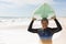 Portrait of smiling biracial senior woman wearing wetsuit carrying surfboard on head at sunny beach