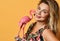Portrait of smiling blonde woman in sundress with tropical print holding pink flamingo figurine on yellow
