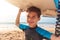 Portrait Of Smiling Boy Wearing Wetsuit Carrying Bodyboards On  Summer Beach Vacation