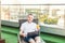 Portrait of smiling businessman with drink working on laptop comfortably sitting on deckchair on office terrace with Urban Landsca