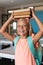 Portrait of smiling caucasian elementary schoolgirl holding stacked books on head in classroom