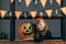 portrait of smiling child in halloween costume at carved pumpkin and hanging flags