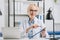 portrait of smiling chiropractor in eyeglasses and white coat pointing at notepad at workplace