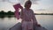 Portrait of smiling confident non-binary trans woman in dress looking at camera shaking pink kerchief sitting in boat